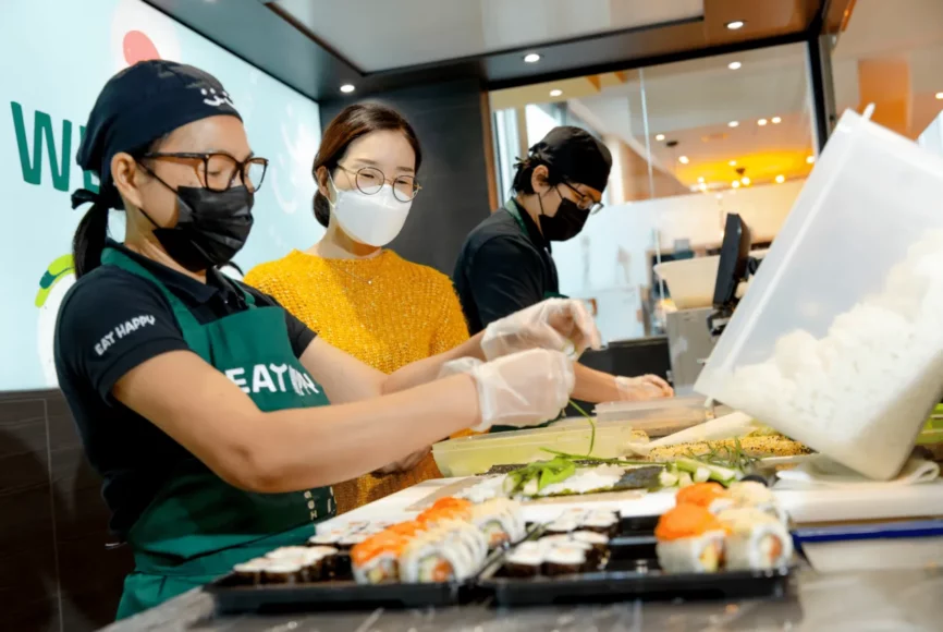 Mitarbeiter mit Masken stellen Sushi im Shop her