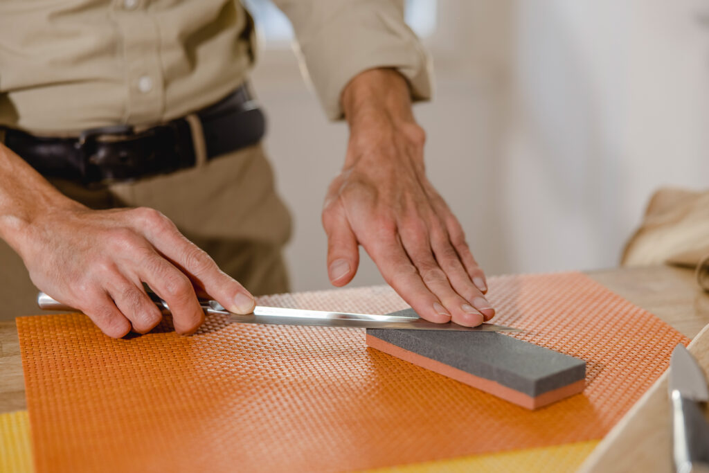 Mann schärft ein Japanisches Küchenmesser mit einem Wetzstein.
